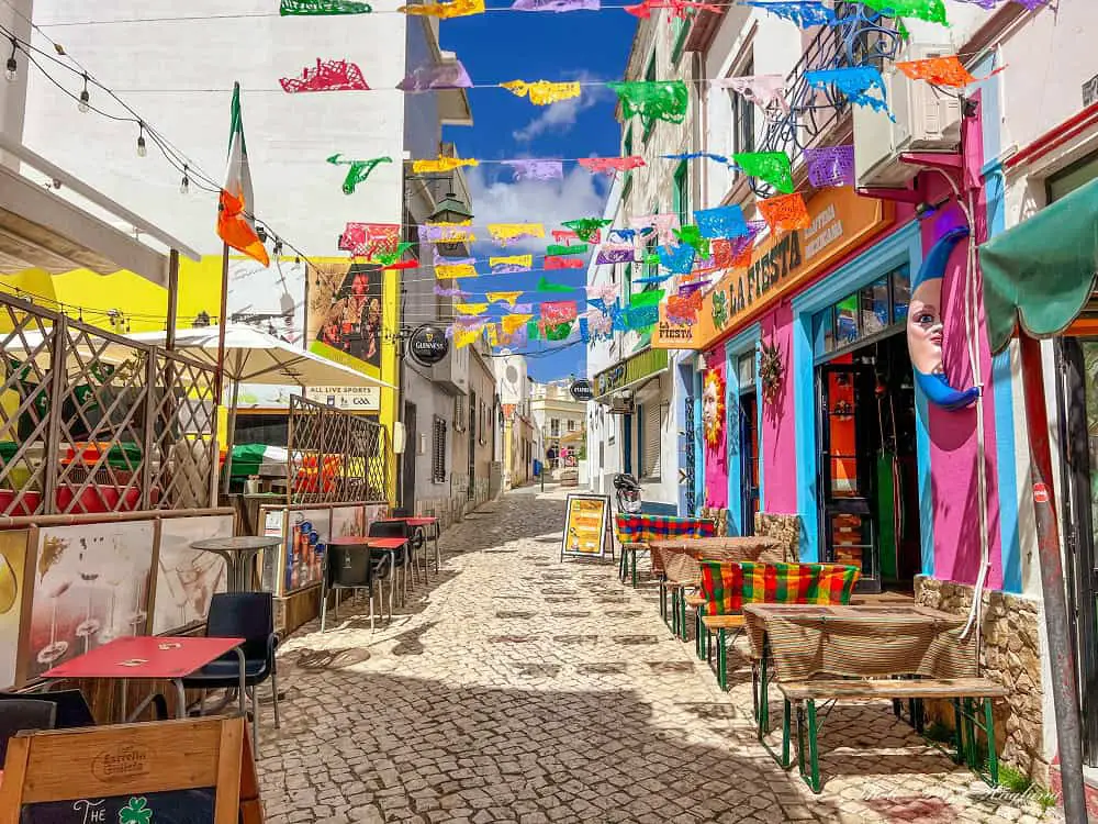 Walking in a cobbled street with colorful bars which is among the best things to do in Alvor Portugal.