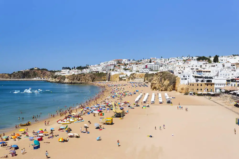 A busy beach with a white village cascading down a cliff - is Albufeira worth visiting